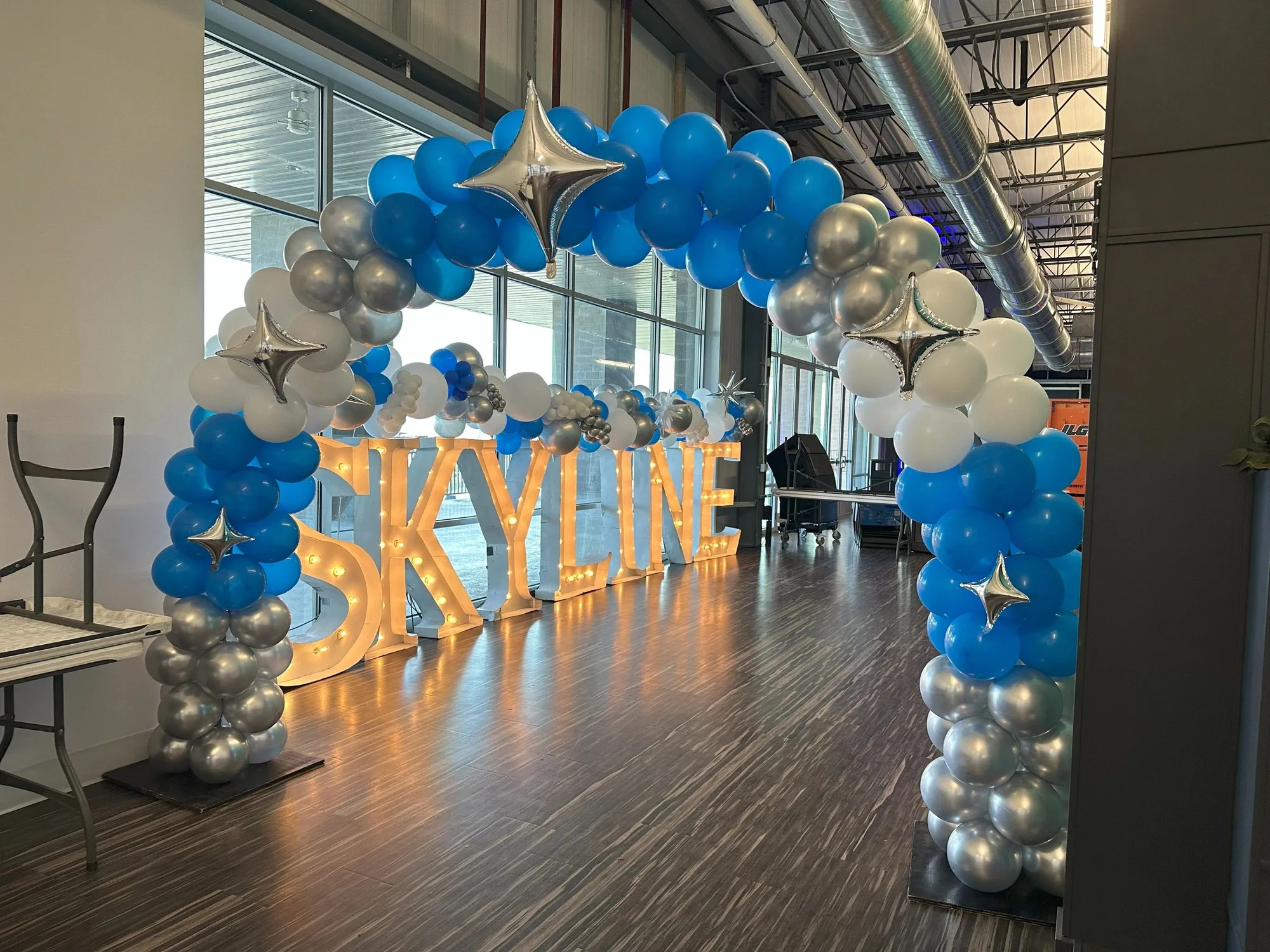 Blue, silver, and white balloon arch in front of illuminated letters
