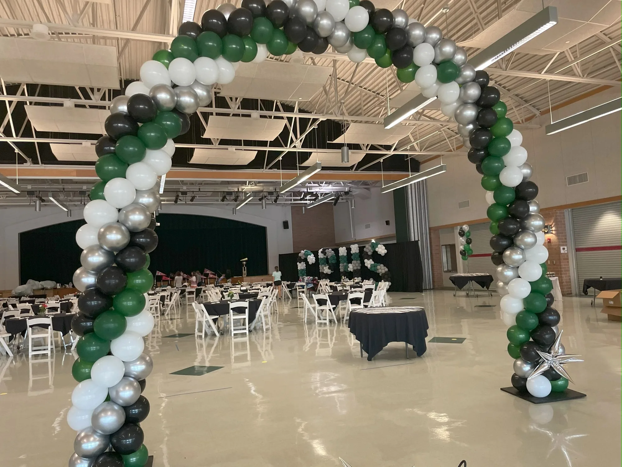 Green, black, silver, and white balloon arch in a large hall